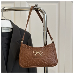 Detail of a brown woven underarm bag featuring a distinctive golden metal bow embellishment