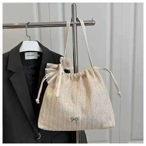 Close-up of beige woven tote bag with metallic bow and lace floral pendant detail