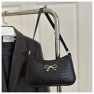 Detail of black woven shoulder bag featuring a delicate gold bow metal buckle and slim strap