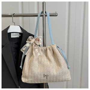Detail of straw tote bag featuring blue drawstring and large floral lace bow accessory