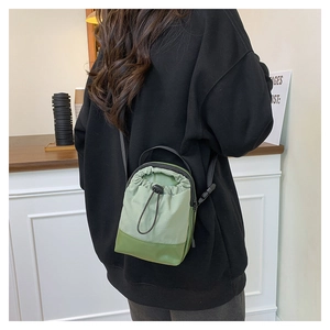 Detail of green nylon drawstring crossbody bag with adjustable black strap worn by model