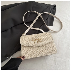 Detail of cream woven straw crossbody bag featuring a decorative gold bow and snap button