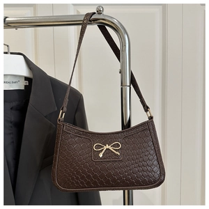 Close-up of a dark brown woven shoulder bag featuring a gold bow hardware clasp