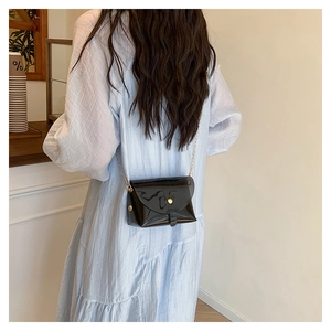 Detail of a black glossy PVC mini bag with a gold chain strap worn by a model in a cafe
