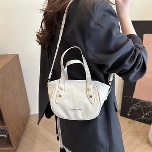 Sac à main en cuir crème avec rivets et bandoulière porté sur un blazer noir