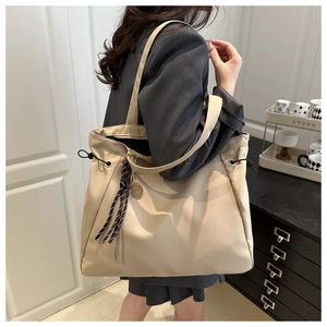 Detail of beige large tote bag featuring drawstring closure and tennis racket pendant