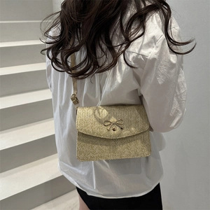 Straw woven crossbody bag with a gold bow accent and leather strap on a model