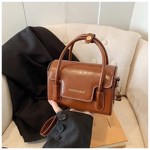 Detail of caramel brown mini square bag with gold lettering and adjustable shoulder strap
