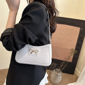 Elegant white woven shoulder bag with gold bow ornament worn by a model in soft lighting