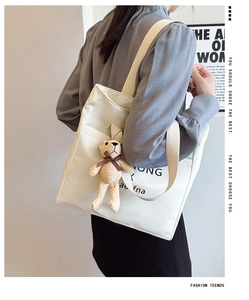 Detail view of white canvas tote bag with black letters and a brown plush bear charm