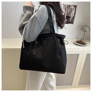 Detail view of a black drawstring nylon tote bag with rope charm on a female model