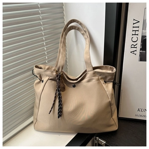 Detail of beige oversized tote bag featuring adjustable drawstrings and metallic ring charm
