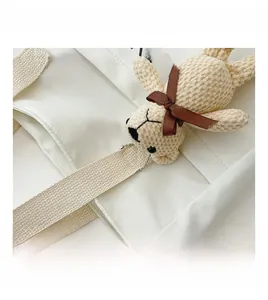 Detail of off-white canvas square bag featuring a corduroy teddy bear charm with bow