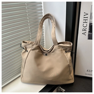 Close-up of beige nylon tote bag featuring side drawstrings and metallic buckle detail