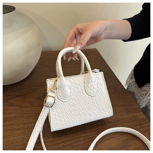 Detailed close-up of a white faux crocodile skin handbag with elegant gold metal hardware