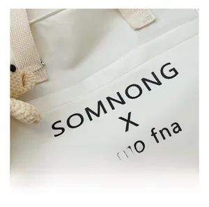 Detail shot of white canvas tote bag with bold lettering and brown plush bear charm