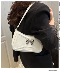 Close-up of white faux leather shoulder bag with geometric embossing and silver metal bow