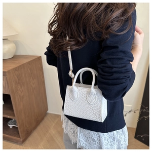 Detail of white mini tote bag with crocodile texture and adjustable crossbody strap