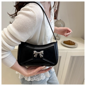 Detail of black glossy faux leather baguette bag with silver metal bow and geometric stitching