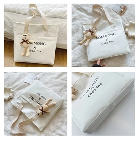 Detail view of large white canvas tote bag with black lettering and a cute bear charm
