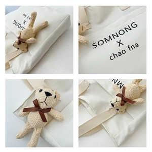 Detail of white canvas tote bag with printed lettering and a cute beige knit bear charm
