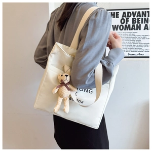 Detailed side view of white canvas tote bag with letter print and brown teddy bear charm