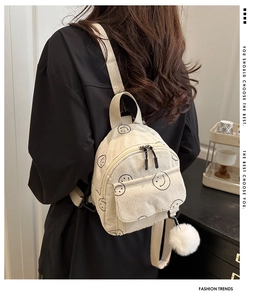 Detail of white corduroy mini backpack featuring a smiley face and plush ball charm
