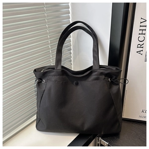 Detail of black nylon tote bag featuring decorative side drawstrings and smooth water-resistant finish