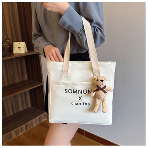 Detail of white canvas tote bag featuring bear pendant and black letter printing