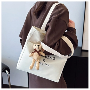 Detail of off-white canvas tote bag with bear charm and wide strap on model back