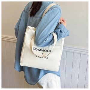 Detail of cream canvas tote bag showing the side view and strap on model shoulder