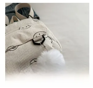 Detailed close-up of corduroy backpack showing smile print and white fluffy pompom charm