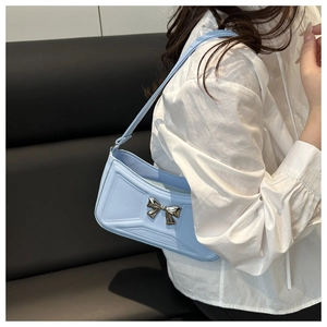 Detail of light blue shoulder bag featuring a 3D textured surface and silver metal bow