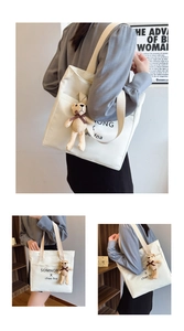Detail of white canvas tote bag with black lettering and cute knitted bear charm