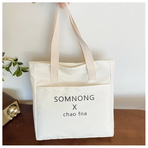 Detail of beige canvas tote bag showing the front slip pocket and printed letter logo