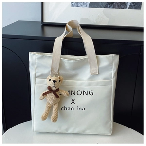 Detail of white minimalist tote bag with text print and a cute knit bear charm