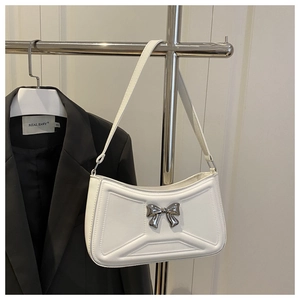 Detailed view of silver bow metal buckle and geometric embossed lines on white leather bag