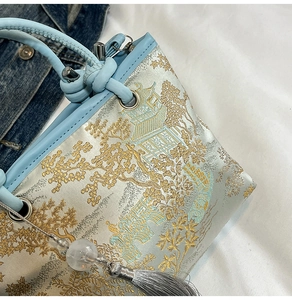 Detailed embroidery of Chinese landscapes on a blue bucket bag with tassel