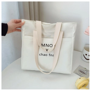 Close-up of white canvas tote bag with black letter print and thick woven handles