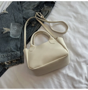 Détail du sac seau blanc crème en cuir grainé posé sur un tissu blanc doux