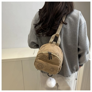 Detail of khaki corduroy mini backpack featuring smiley face print and white plush charm