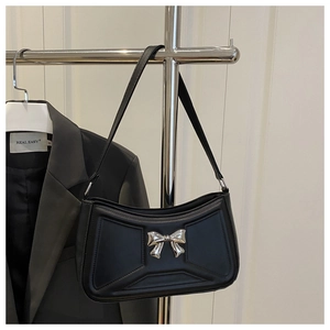 Close-up of black glossy shoulder bag featuring a silver metal bow accent on minimalist leather