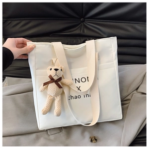 Close-up of canvas tote bag with letter print and cute teddy bear charm on grey blazer
