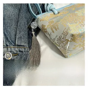 Detail of light blue embroidered bucket bag with gold floral patterns and gray tassel charm