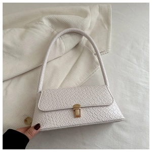 Gros plan sur la texture cuir crocodile blanc et le fermoir en métal doré d'un sac à rabat