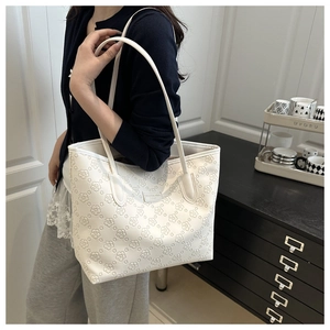 Detailed view of a white floral embossed tote bag with brand name worn by a model