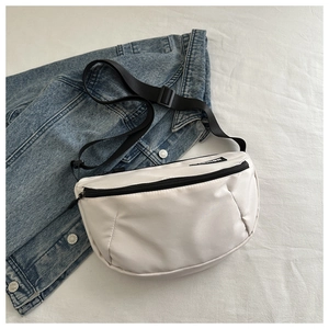 Détail du sac bandoulière demi-lune en nylon blanc avec fermeture éclair noire sur denim