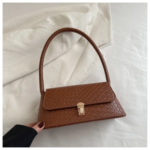 Détail d'un sac marron à texture tressée avec boucle dorée sur fond de velours côtelé