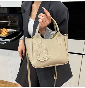 Détail d'un sac seau en cuir beige avec charm de chiot tenu par un mannequin en cuisine