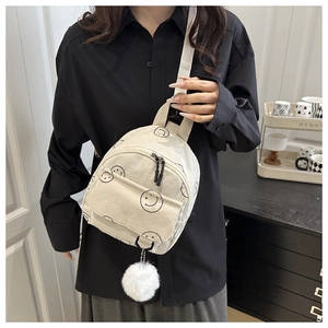 Detail eines cremefarbenen Cord-Rucksacks mit Smiley-Muster und flauschigem Bommel-Anhänger